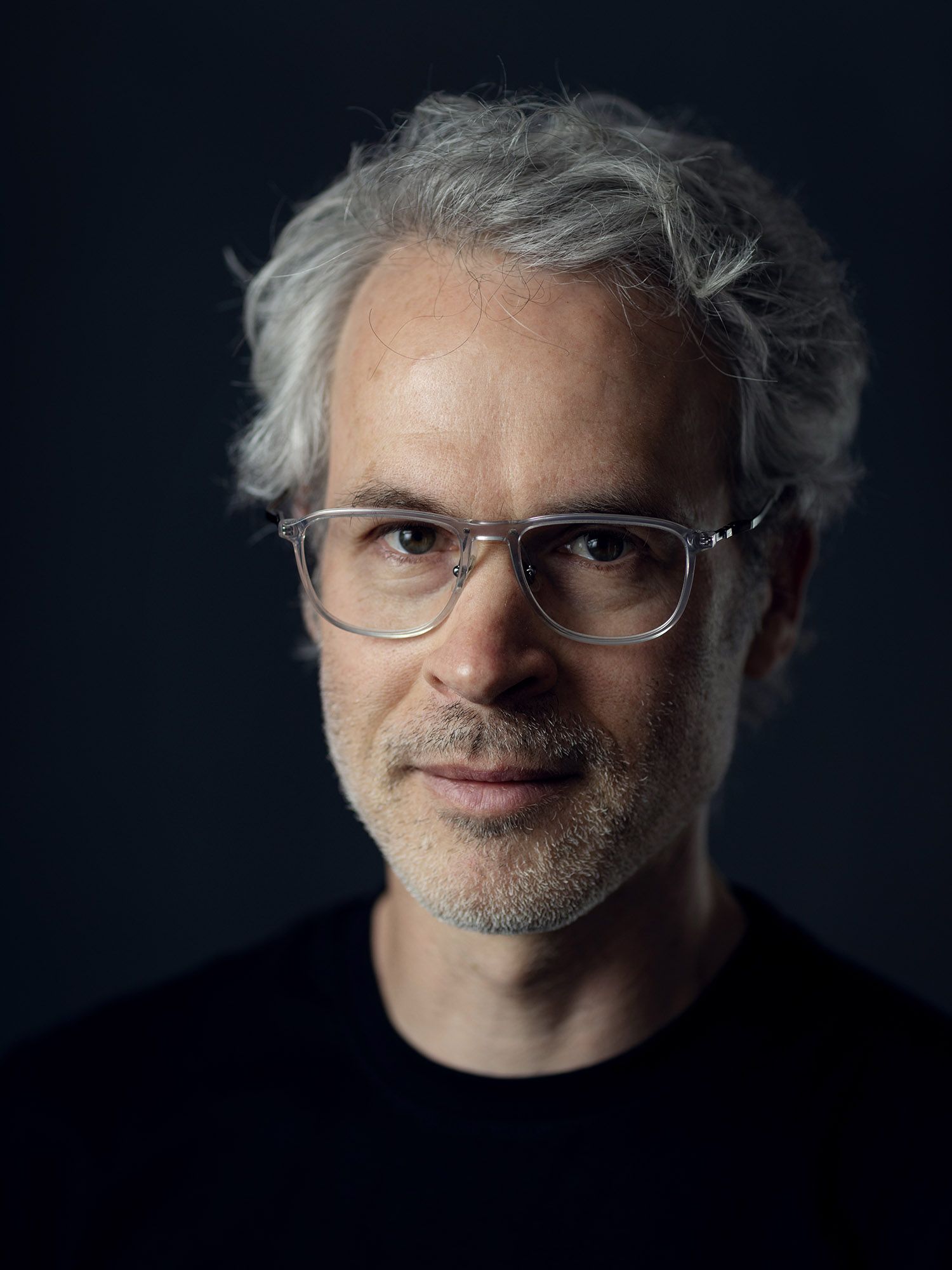 Dramatic low-key portrait with glasses against dark background.