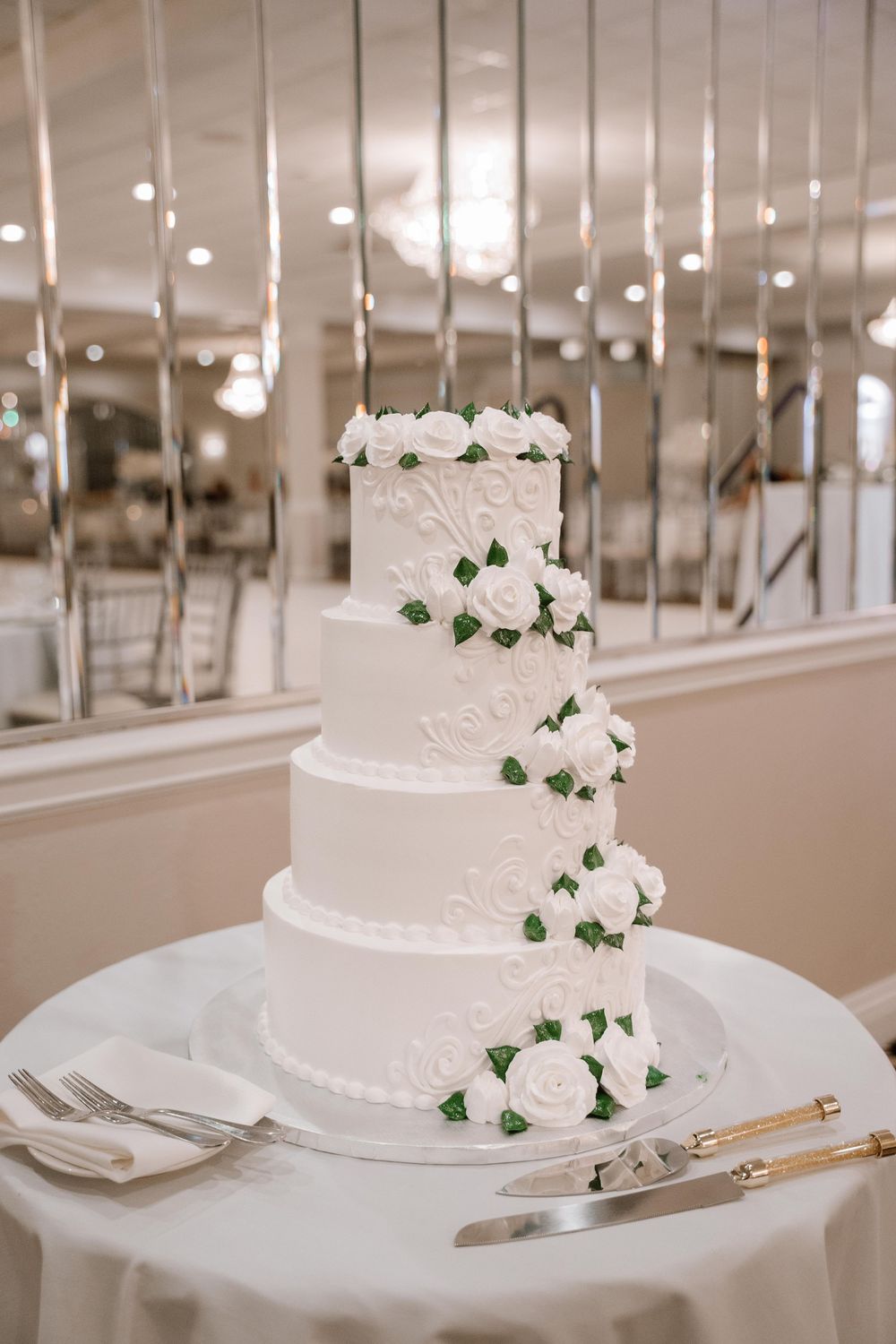 Elegant white tiered wedding cake decorated with delicate green ivy and roses on a classic silver cake stand.