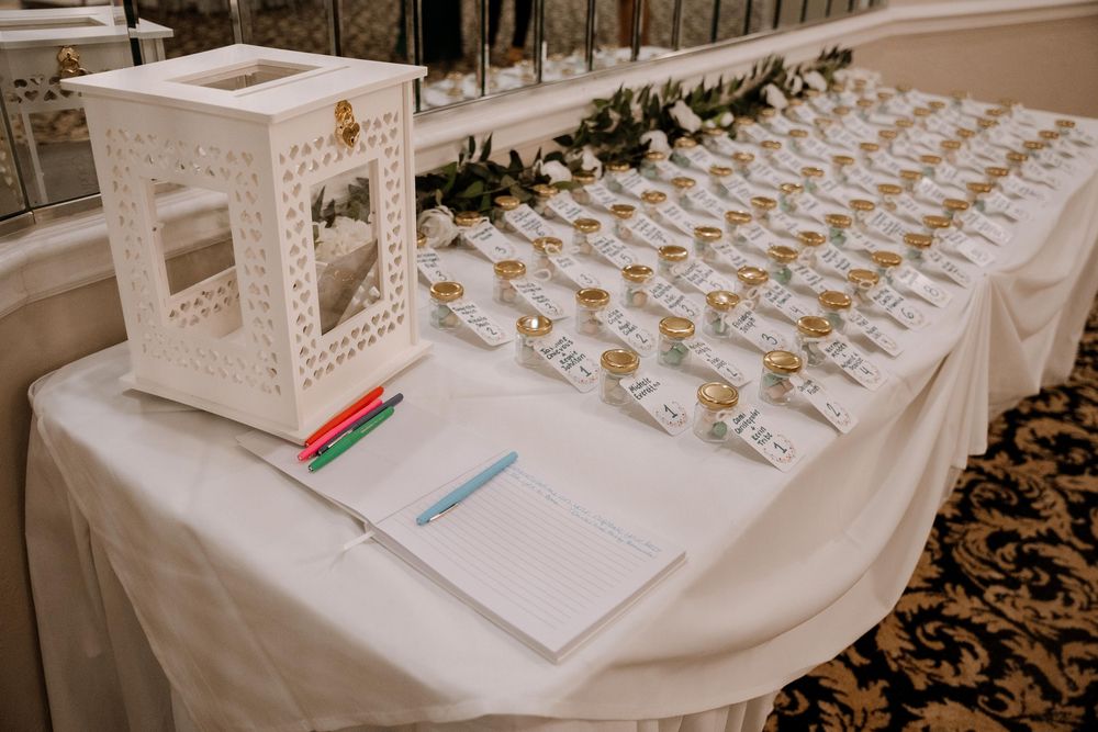 Wedding reception venue with elegant place card display featuring white cards arranged on white tablecloths.