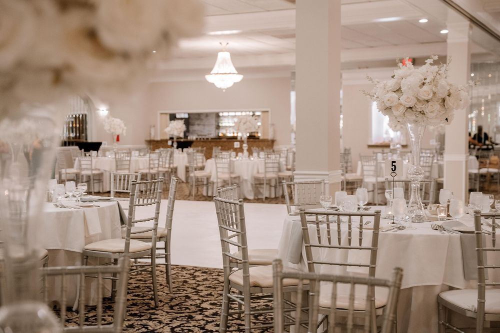 Elegant wedding reception ballroom with white linens and silver chiavari chairs arranged at round tables.