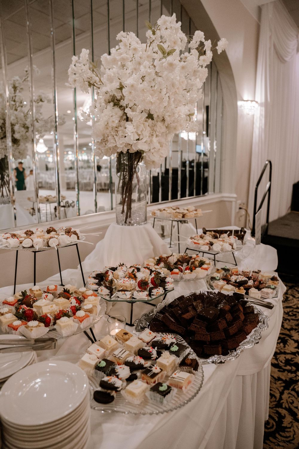 Elegant wedding reception buffet table with white floral arrangements and crystal chandeliers in a luxurious ballroom setting.