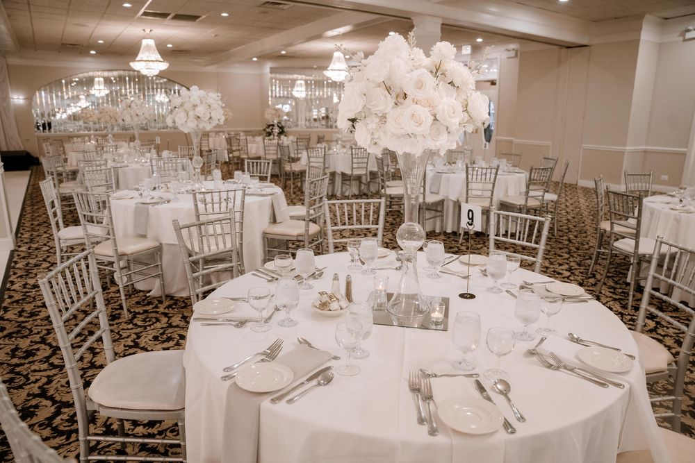 Elegant wedding reception venue with white chiavari chairs and crystal chandeliers creating a romantic atmosphere.