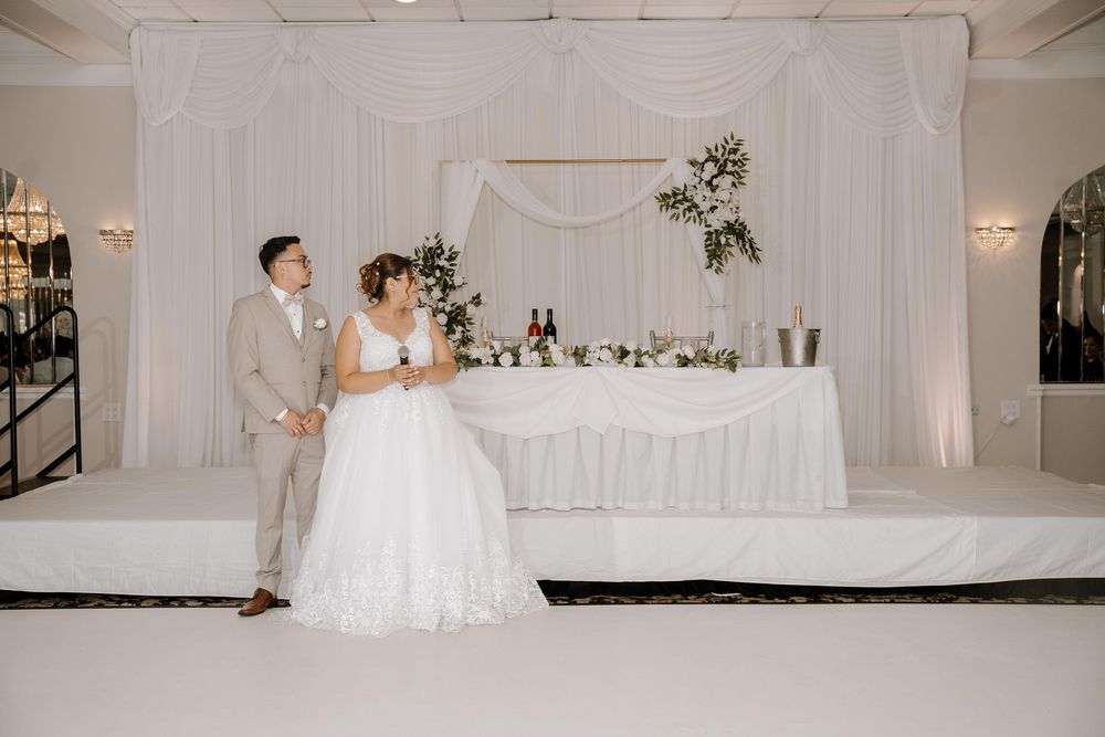 White wedding reception venue with elegant decor, tables, and romantic lighting.