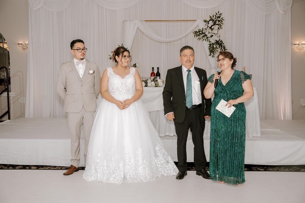 A group of wedding guests in formal attire celebrate and dance together in an elegant white reception venue.