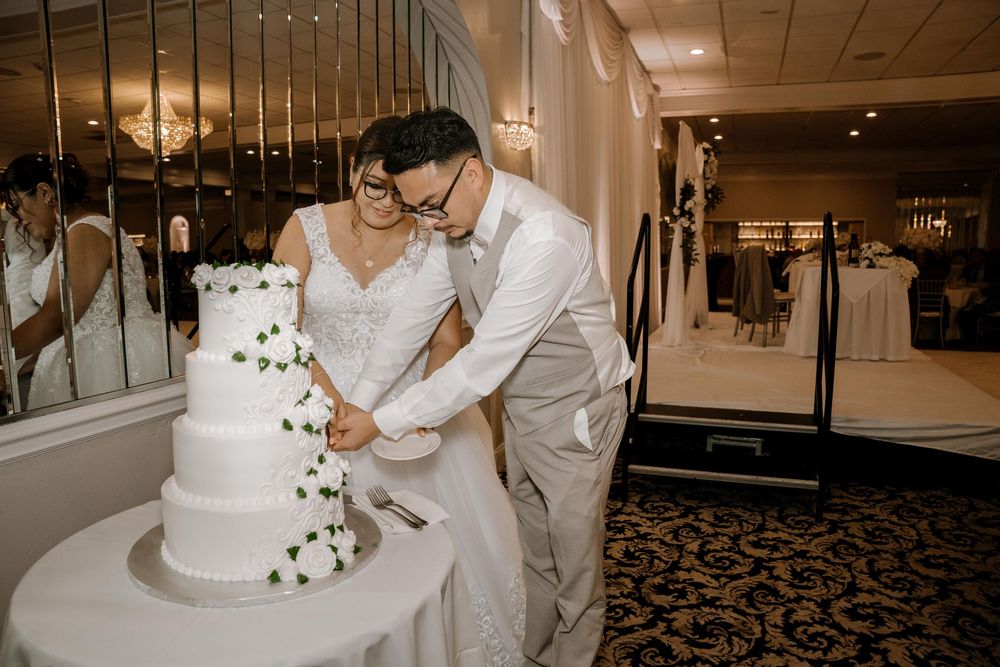 A couple cuts their elegant white wedding cake decorated with delicate floral accents at an indoor reception.