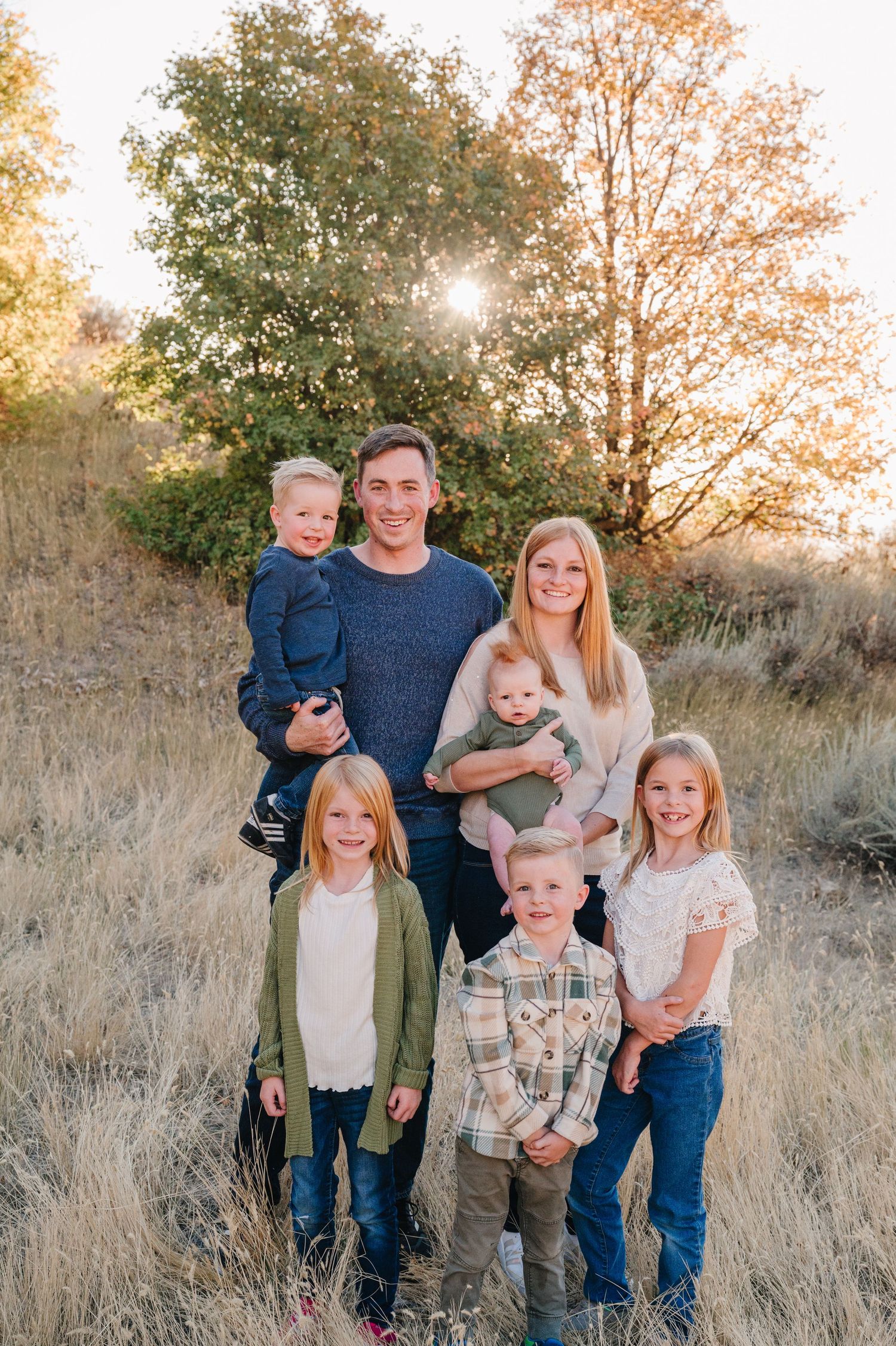 A family poses together in a field of tall grass during golden hour at sunset.