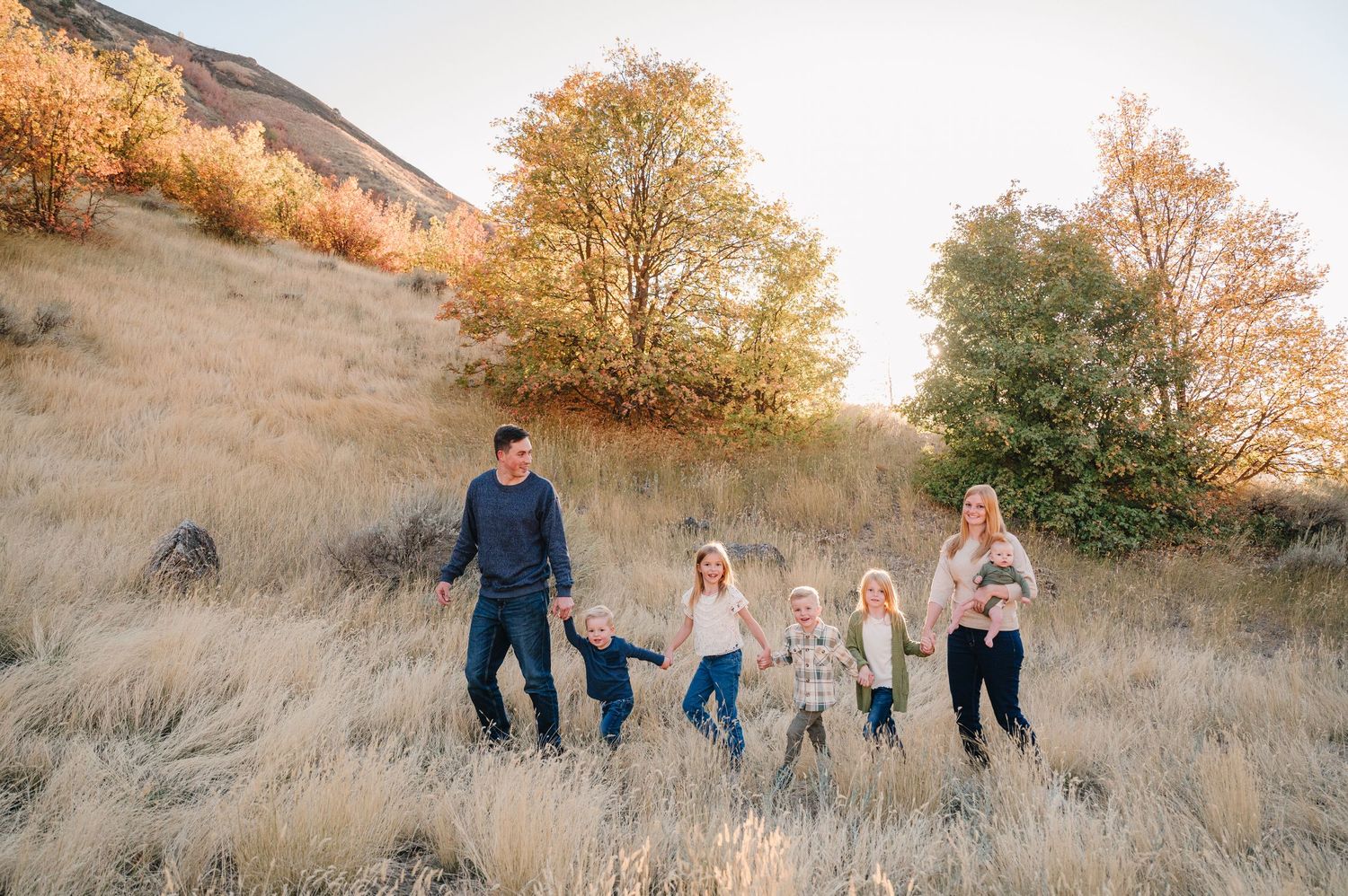 Family walking together on a golden hillside during sunset in matching blue outfits.