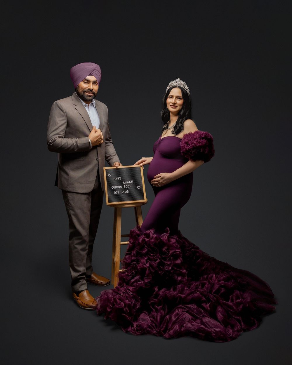 A romantic maternity photo shoot in a dark studio with a flowing purple ruffled dress and chalkboard sign.