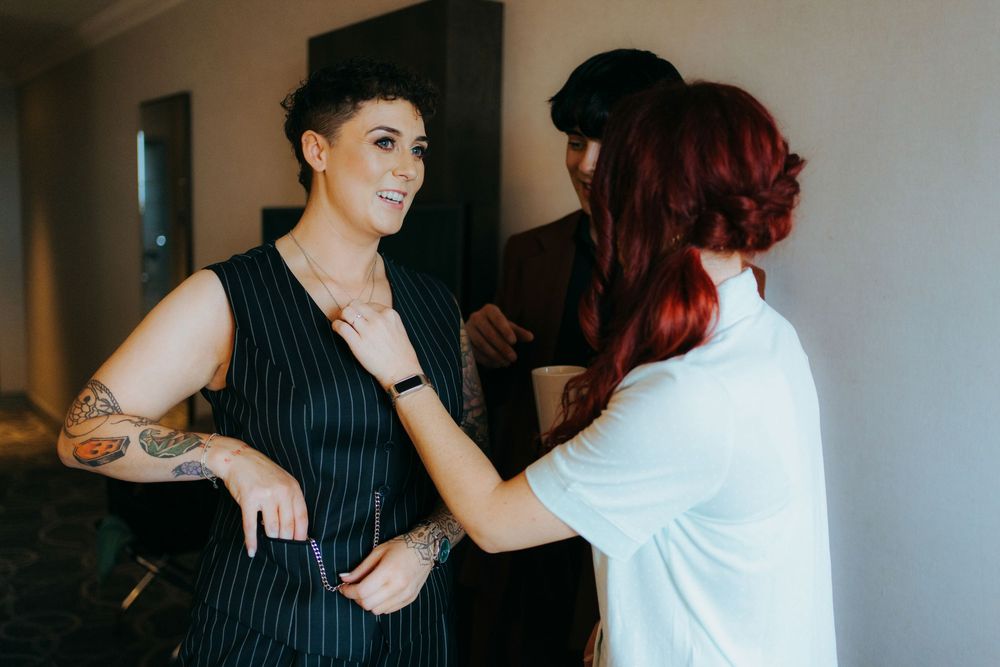 A stylist in a white shirt adjusts a pinstripe vest on someone during a fitting session.
