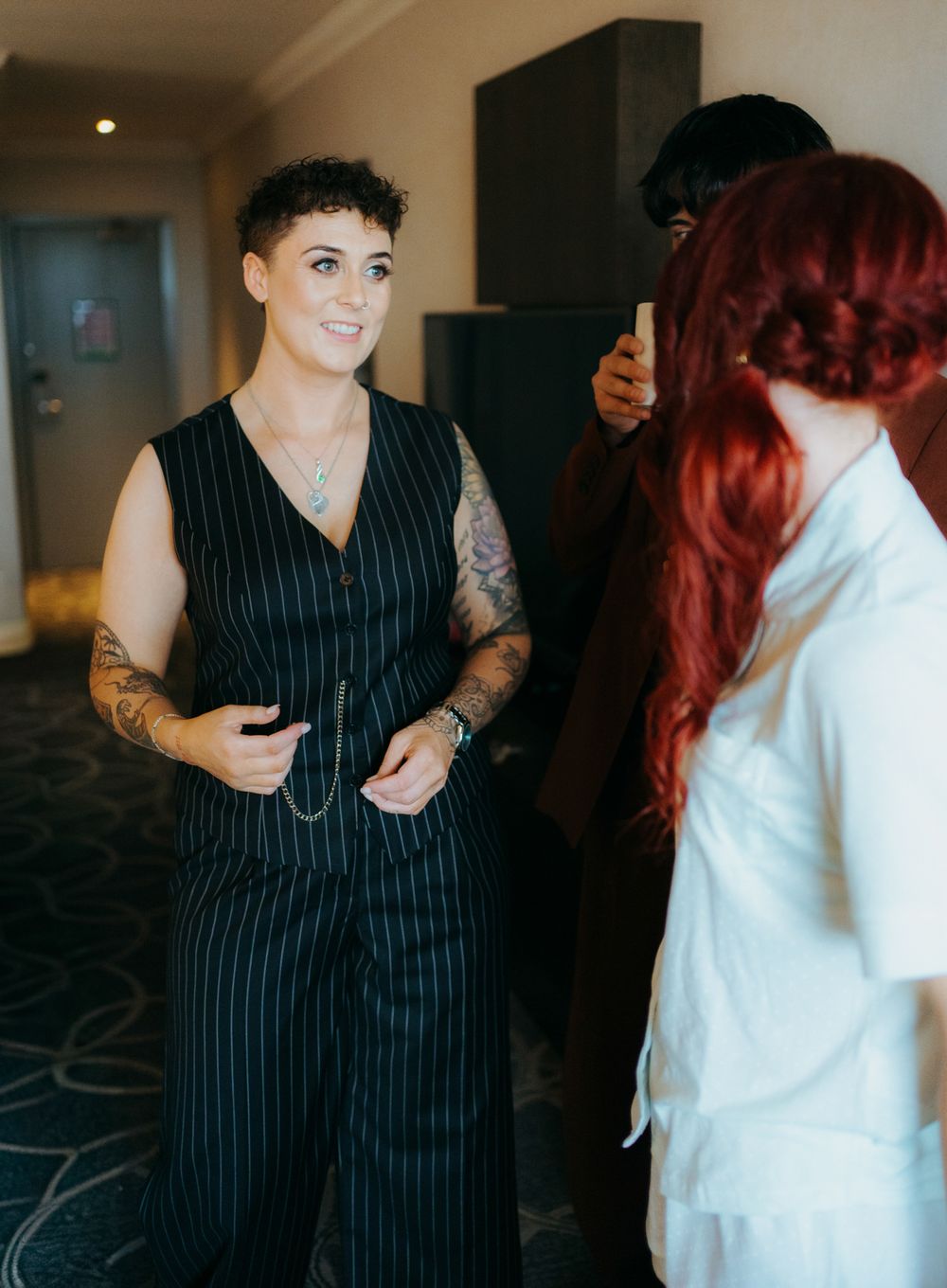 Two people interact in an indoor setting, one wearing a black pinstripe dress and the other in white attire.
