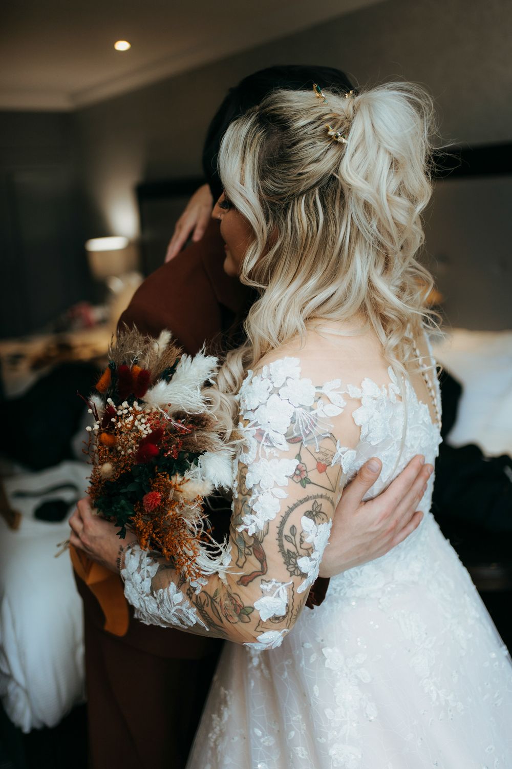 Close-up view of a white wedding dress with delicate floral lace details and autumn-colored bouquet.