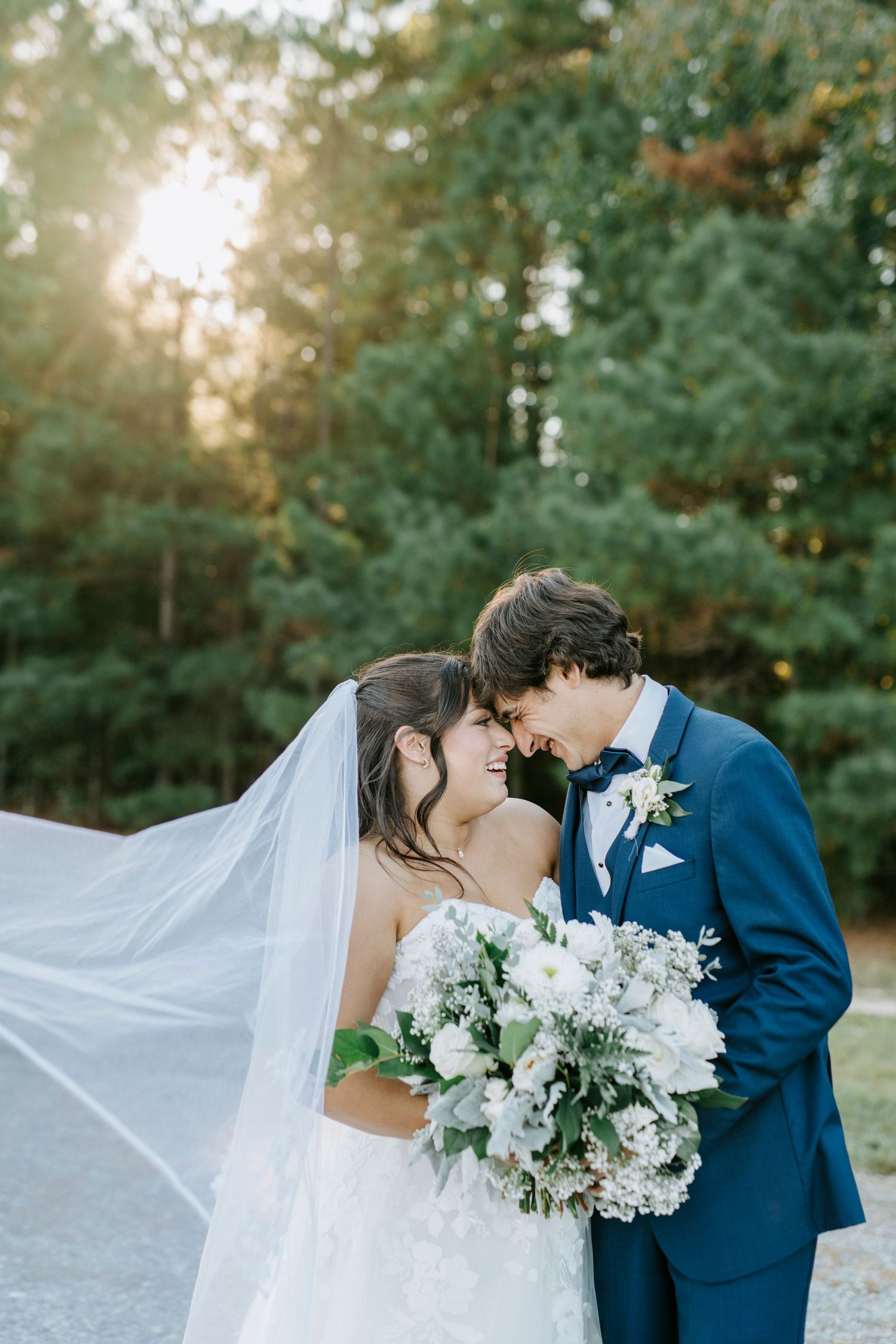 Romantic wedding couple shares intimate moment in outdoor garden setting with flowing veil and white bouquet.