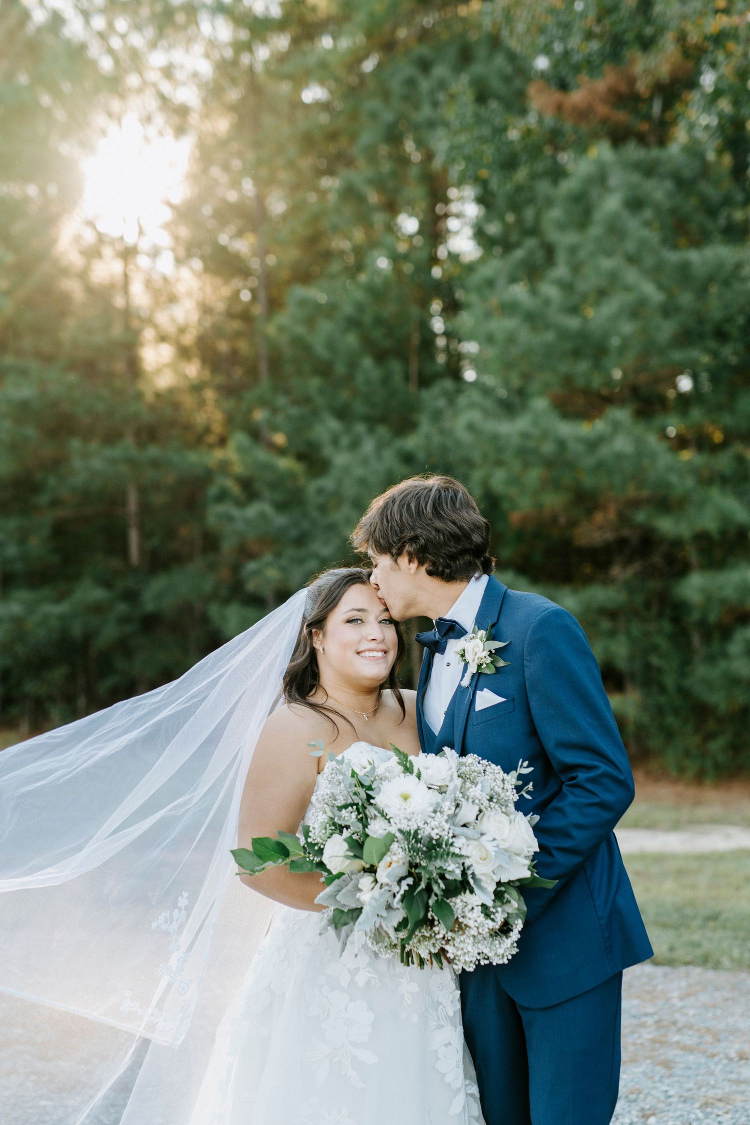 Bride and groom share romantic moments in a sunlit garden setting with flowing veil and white bouquet.
