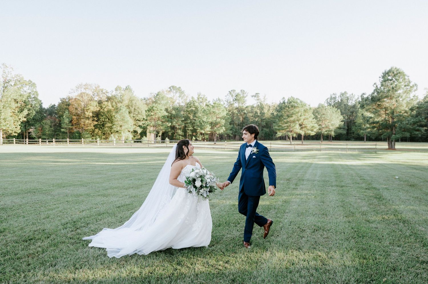 A wedding couple walks together across a lush green field on their special day.