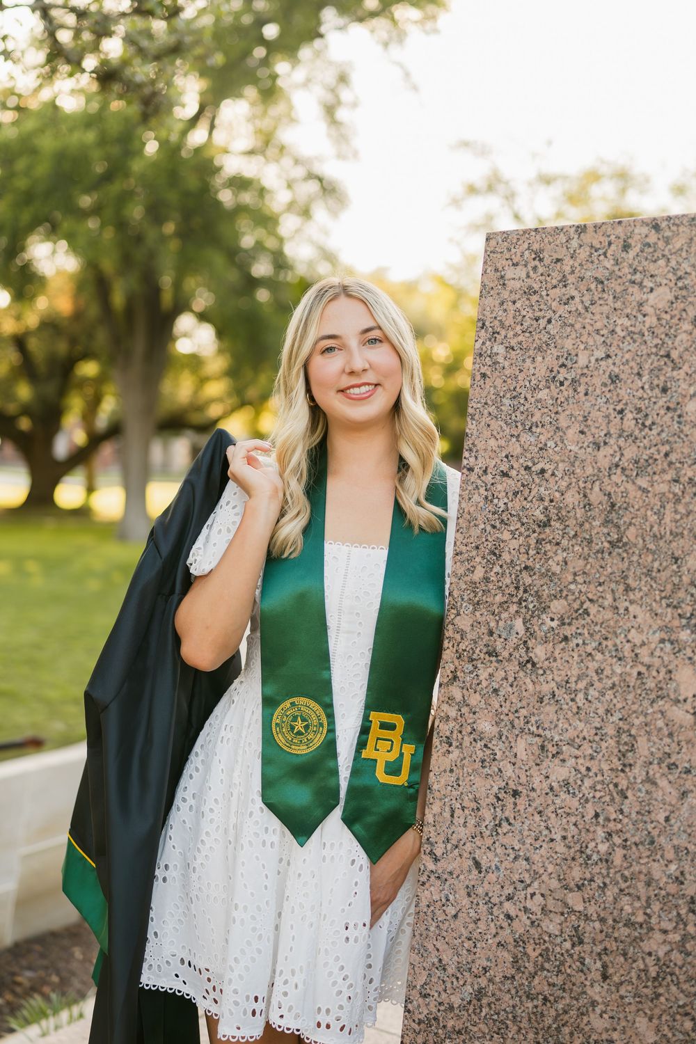 Smiling blonde woman holding graduation gown with Baylor University stole beside Judge Baylor.