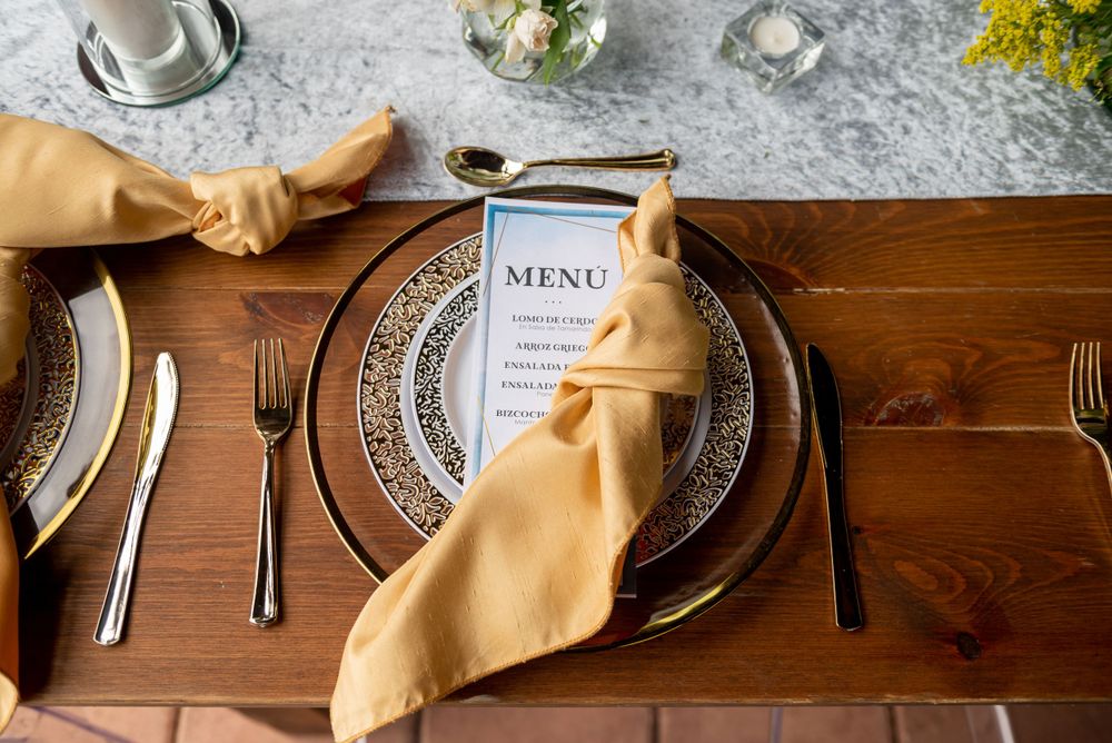 Wedding table setting with gold napkins, floral centerpiece and classic white plates.