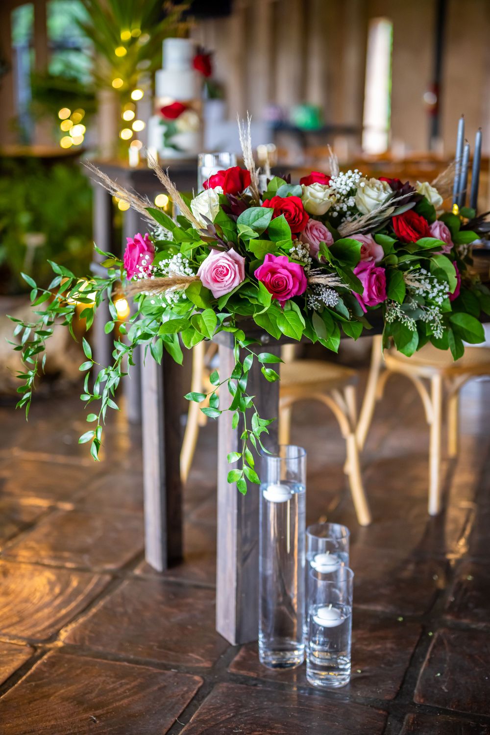 Vibrant floral centerpiece with red and pink roses arranged with greenery on wooden table.