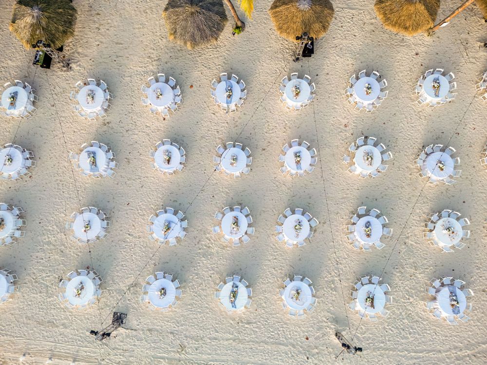 Aerial view of beach umbrellas and chairs arranged in symmetrical rows on sandy shore.
