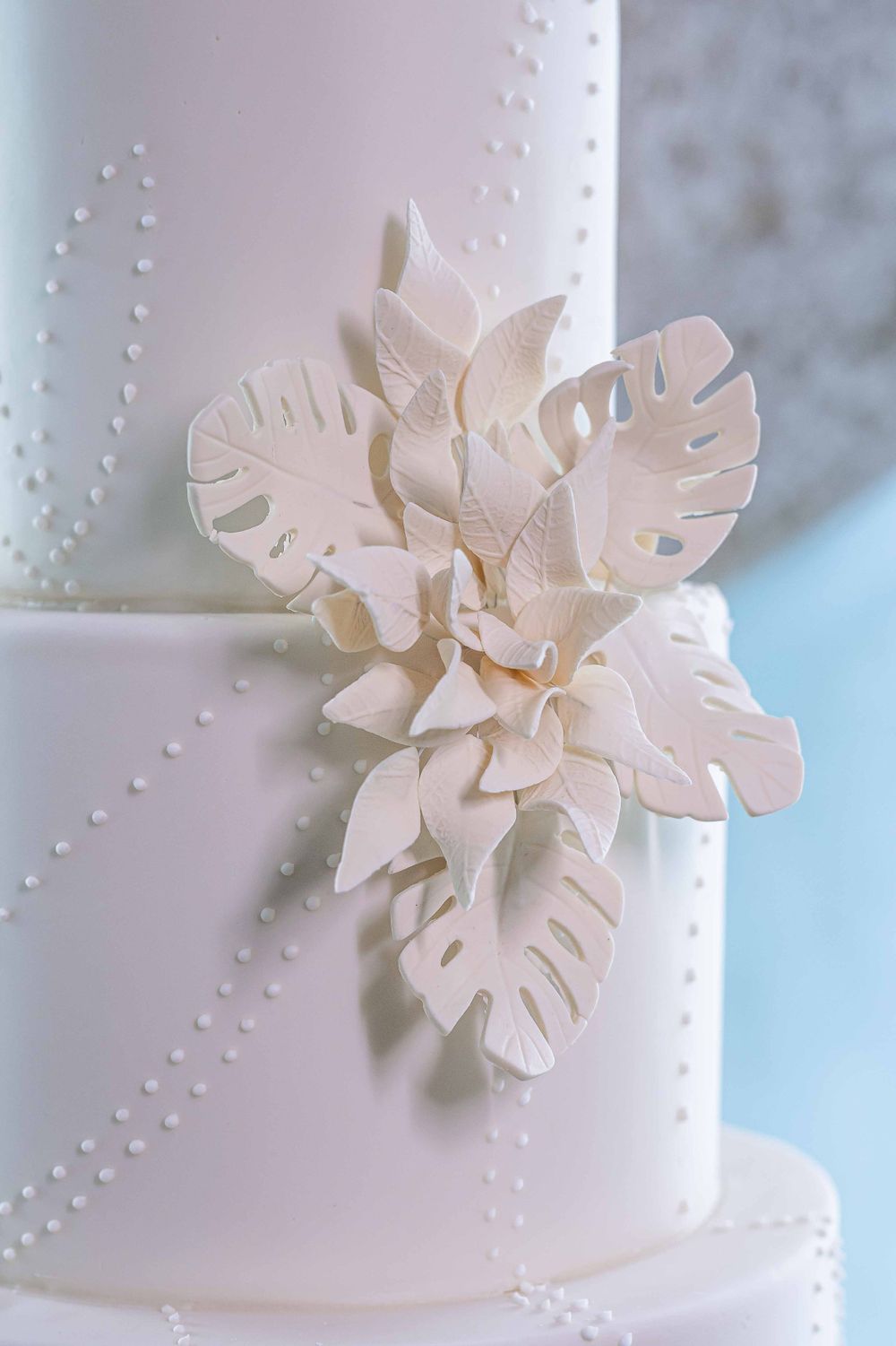 Delicate white sugar flower and tropical leaf detail on a wedding cake.