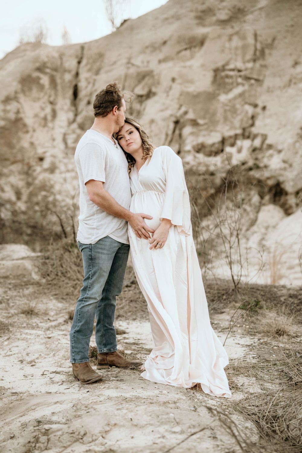 Couple shares an intimate moment against rocky cliffs in matching white outfits.