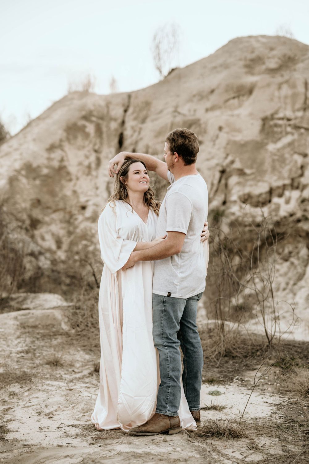 Couple in white and casual wear embrace tenderly against a rocky landscape.
