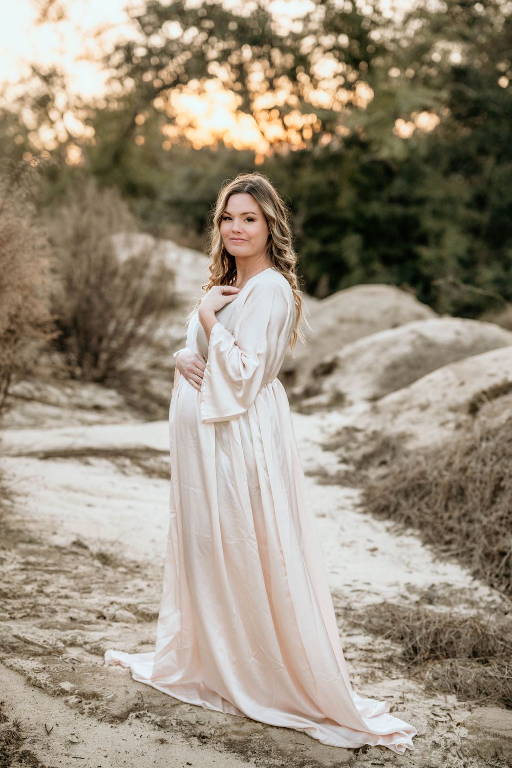 Person in flowing white dress poses during sunset in a natural rocky setting.