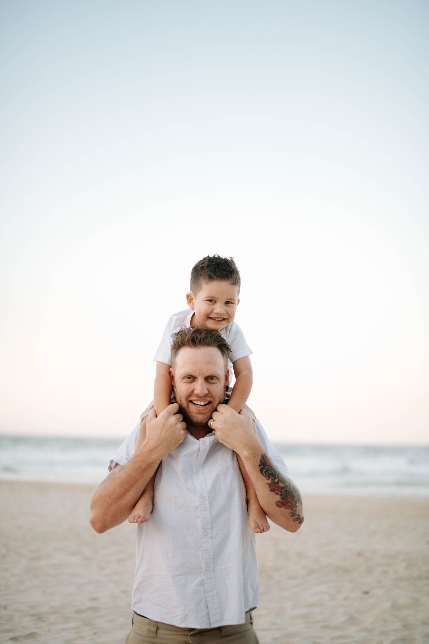 A joyful seaside moment captured at the beach with a child riding on shoulders during sunset.