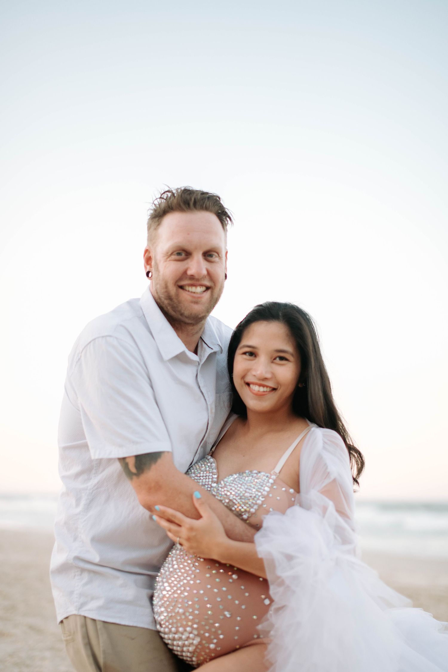 Heartwarming beach maternity photo with a glowing pregnant woman in a sparkly dress.