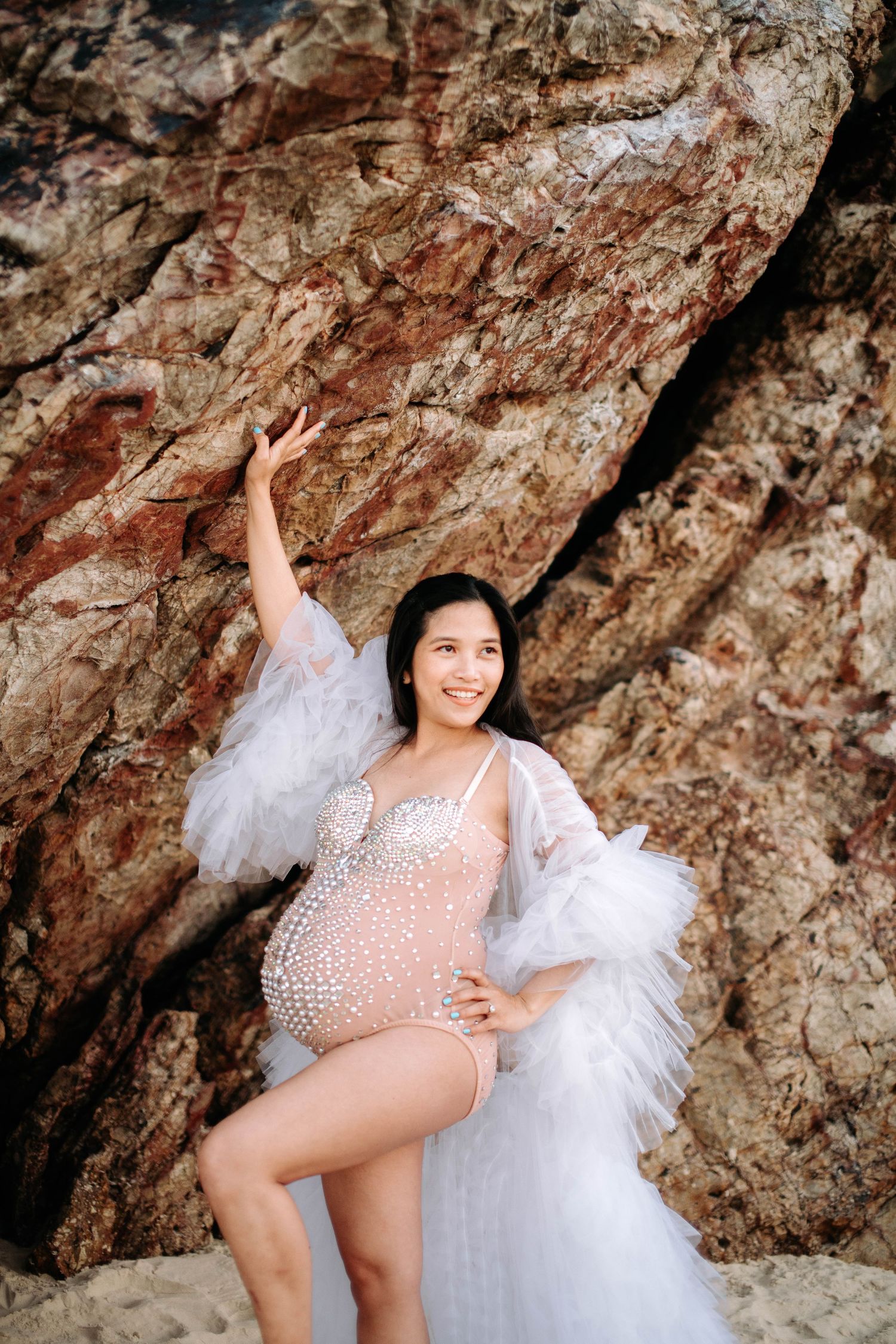 Maternity shoot featuring a sparkly dress against dramatic rocky beach cliffs.