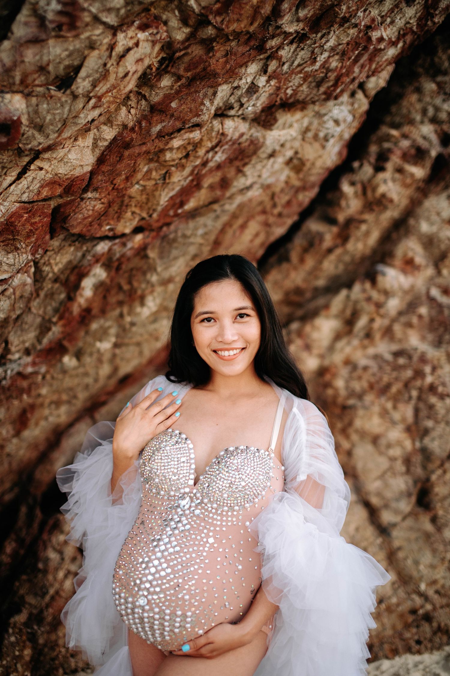 Glowing expectant mother in sequined dress poses against textured rock face.
