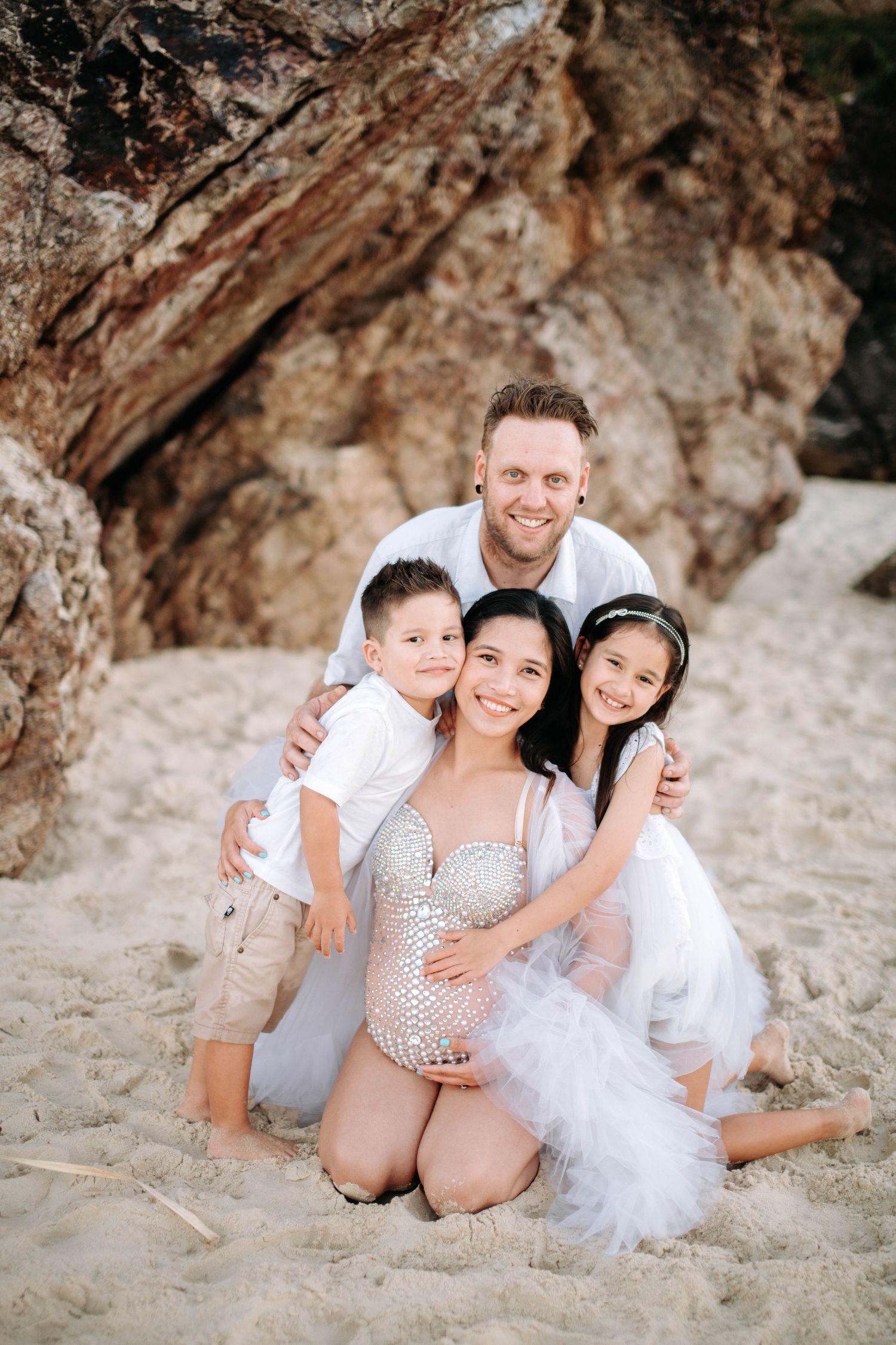 Intimate family beach portrait against rocky backdrop during sunset.
