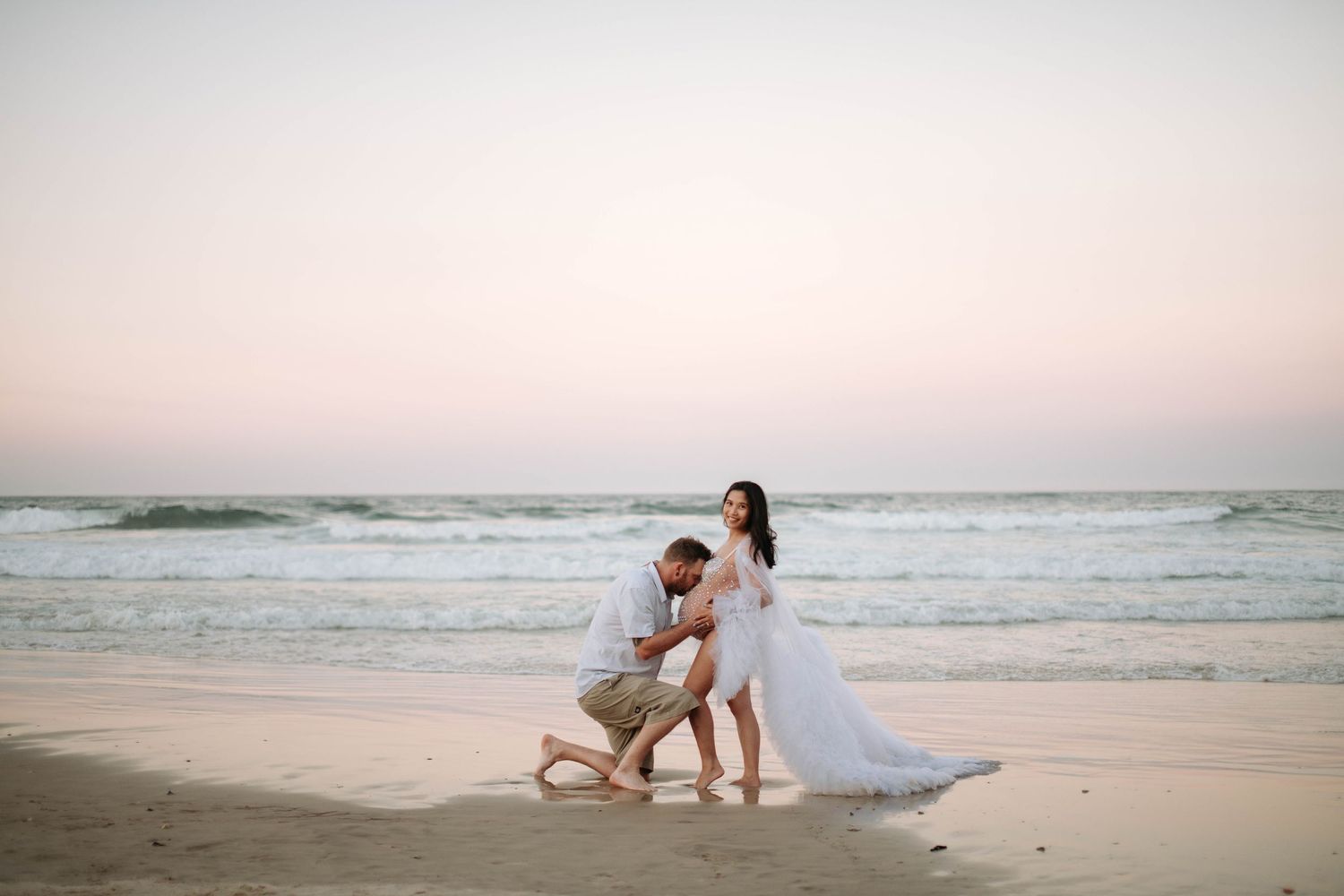 Romantic beach scene with couple during sunset maternity photoshoot.