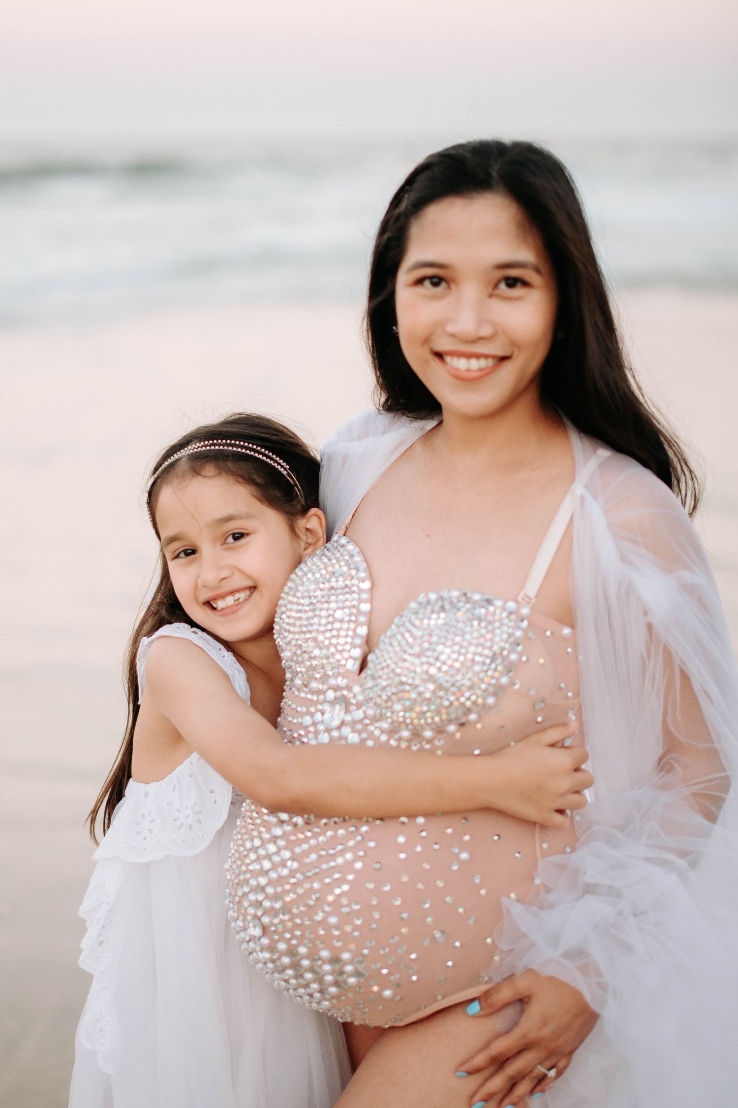 Sweet beach portrait featuring matching white dresses against sunset backdrop.