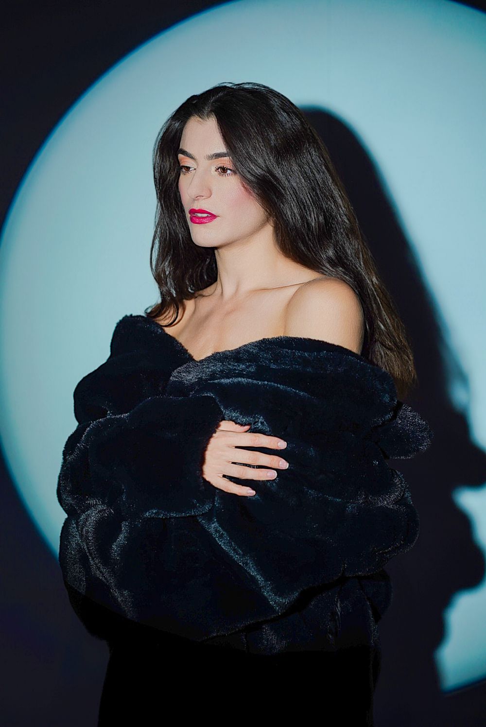 Glamour shot featuring a black fur coat against turquoise backdrop with dramatic lighting.