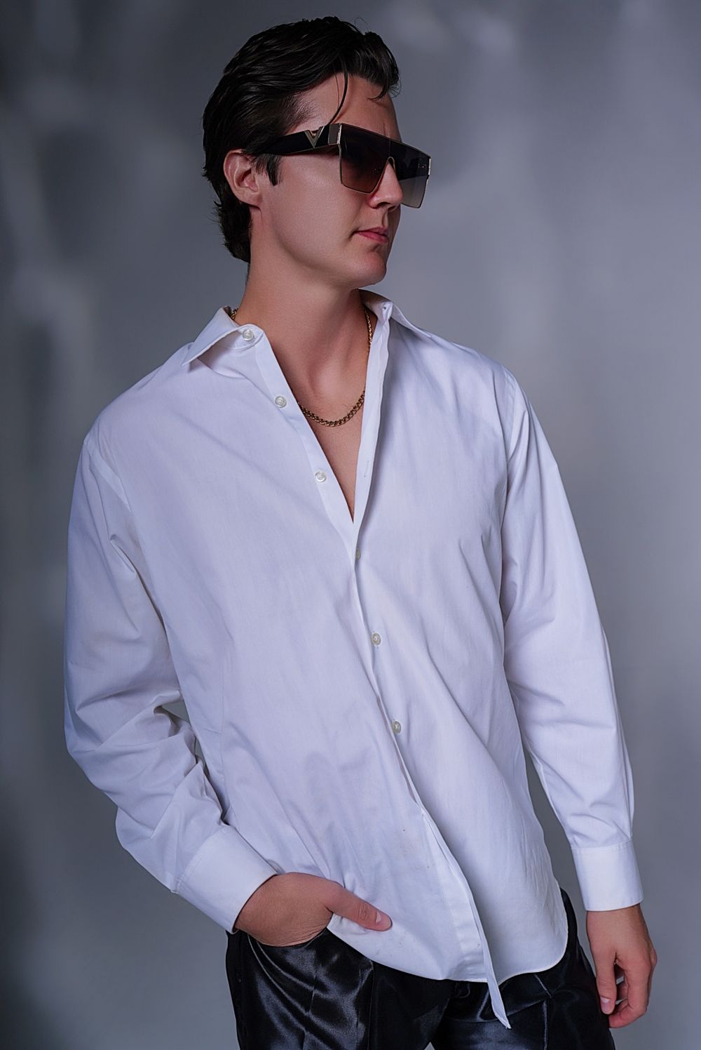 Dramatic studio portrait of a model in white button-down shirt and sunglasses against grey background.