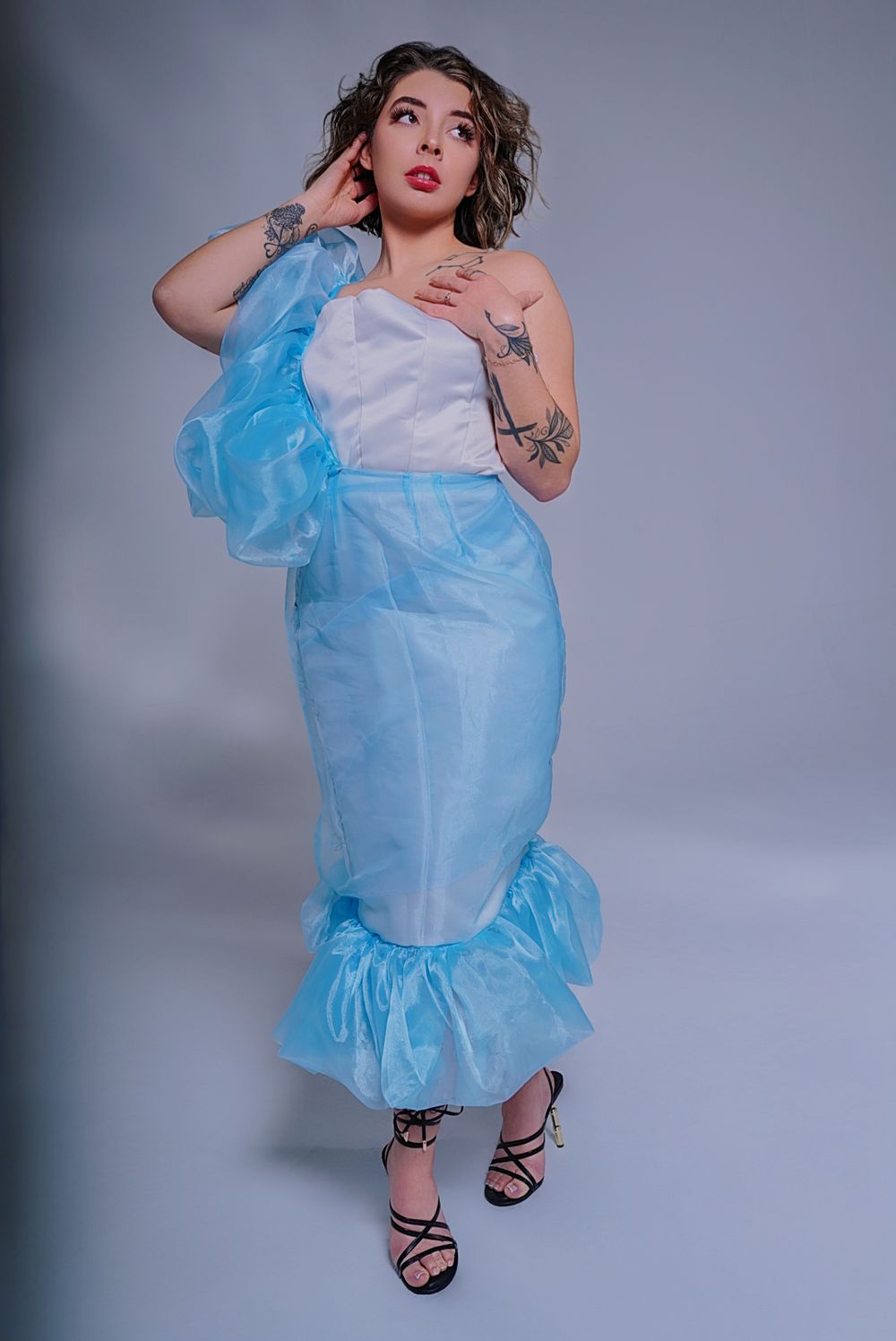 Model wearing a flowing light blue and white dress with ruffles in a studio setting.