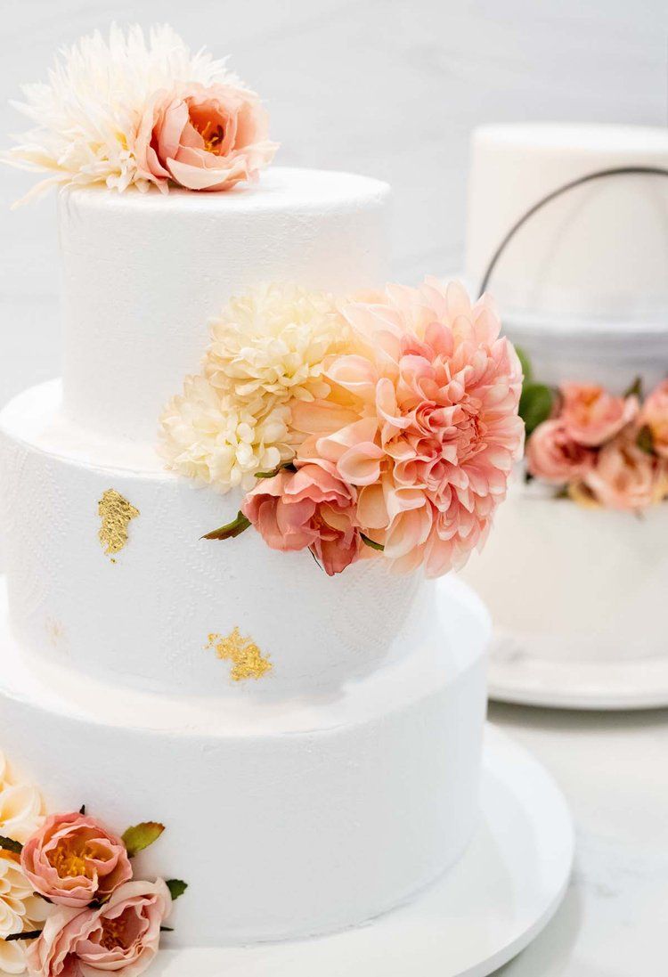 Elegant white tiered wedding cake decorated with delicate peach and coral flowers and gold leaf accents.