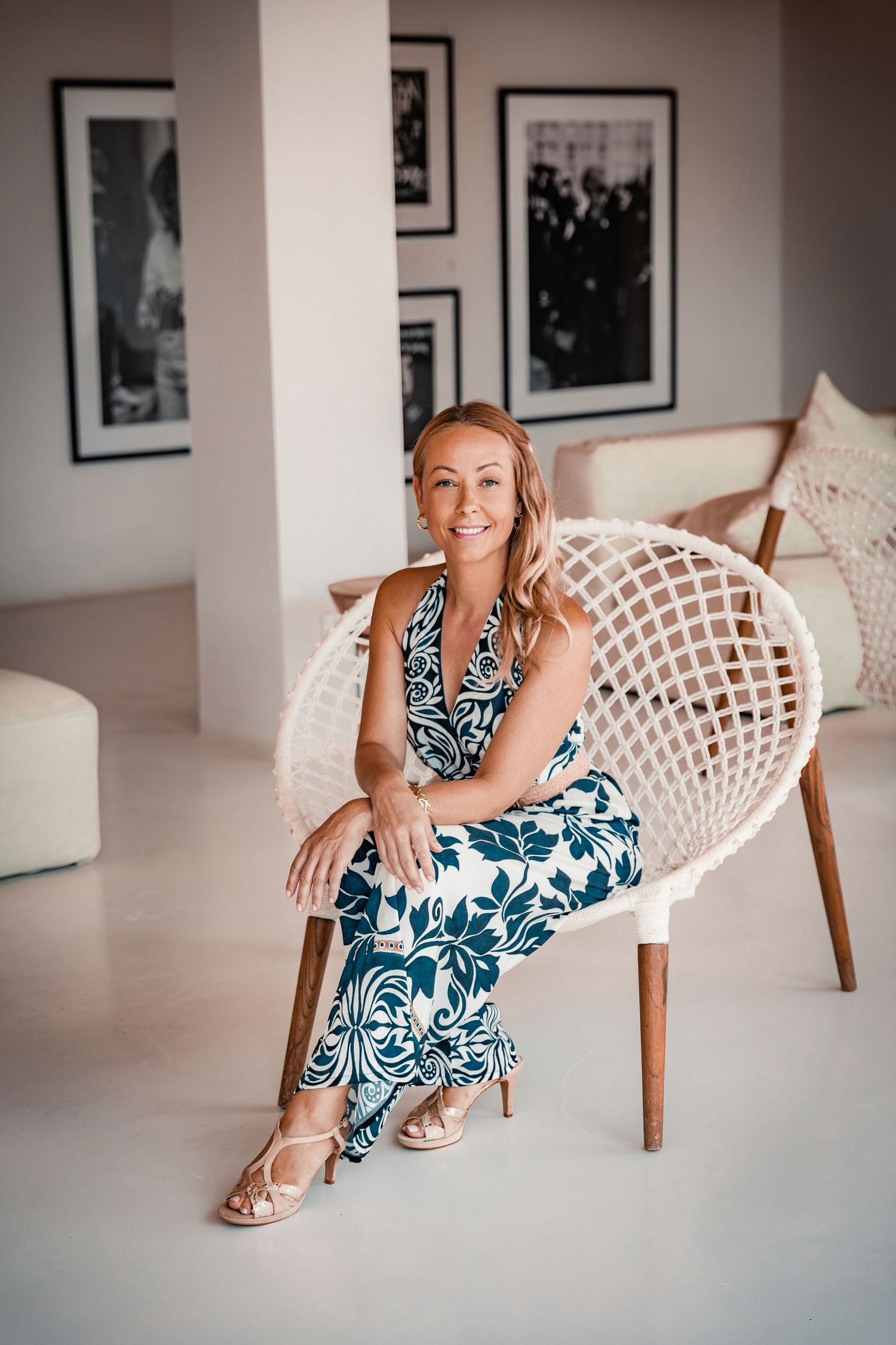 Woman smiling sitting on a modern white basket seat in a floral summer dress at beach club NU Mallorca, Playa de Muro.