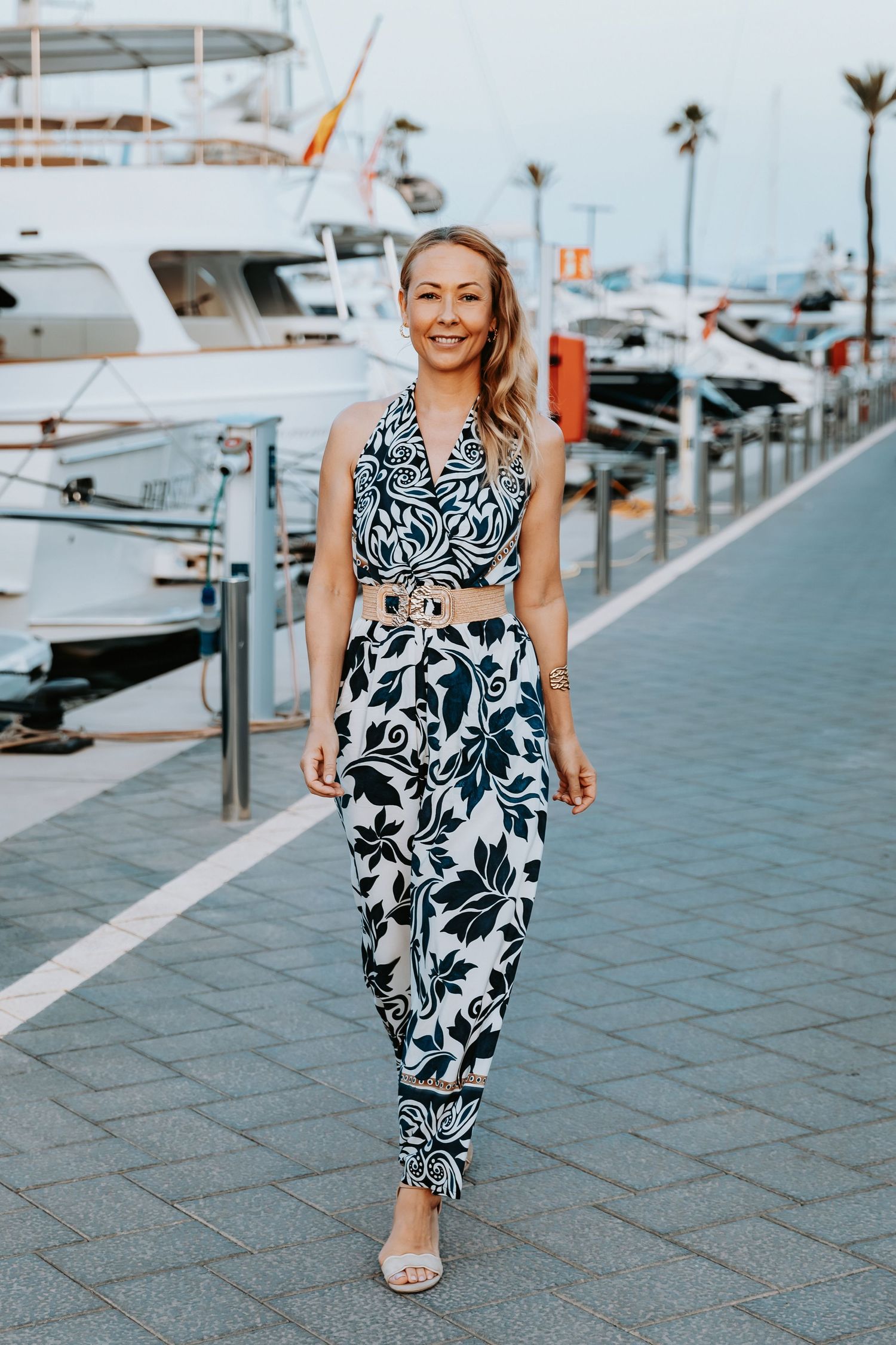 Full length portrait of a woman wearing a floral dress outfit walking along the marina docks.