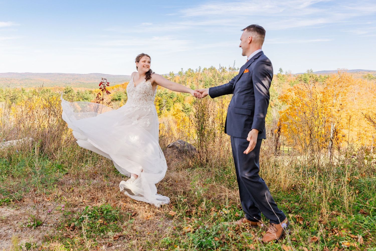 Playful wedding photo with bride's dress flowing in autumn field.