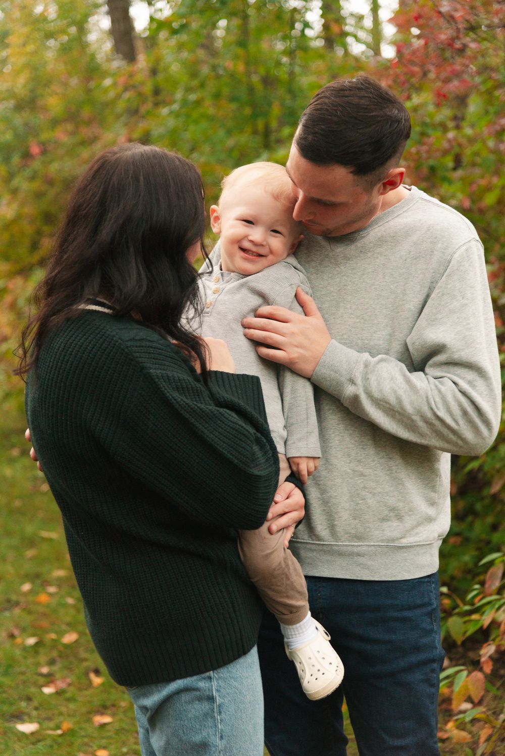 Sweet family moment captured outdoors with fall colors in the background.
