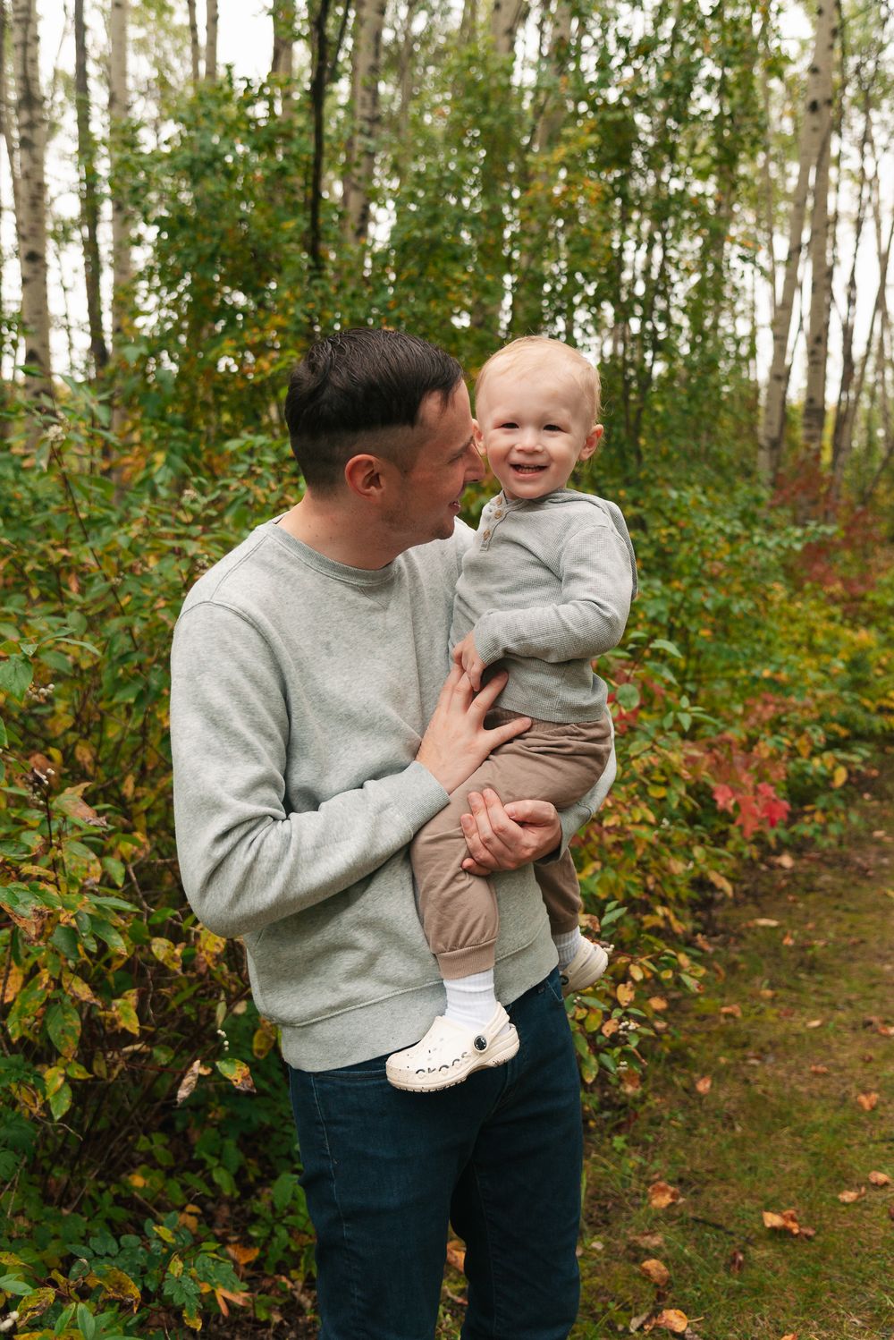 Playful moment between parent and toddler in a fall forest setting.