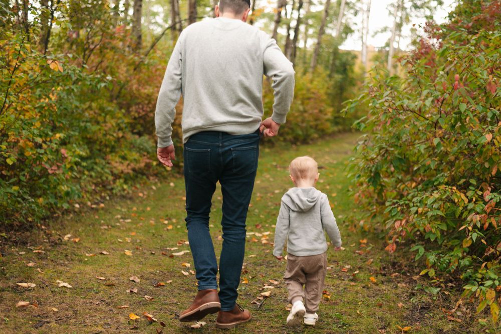 Parent and child walking together on an autumn forest path.