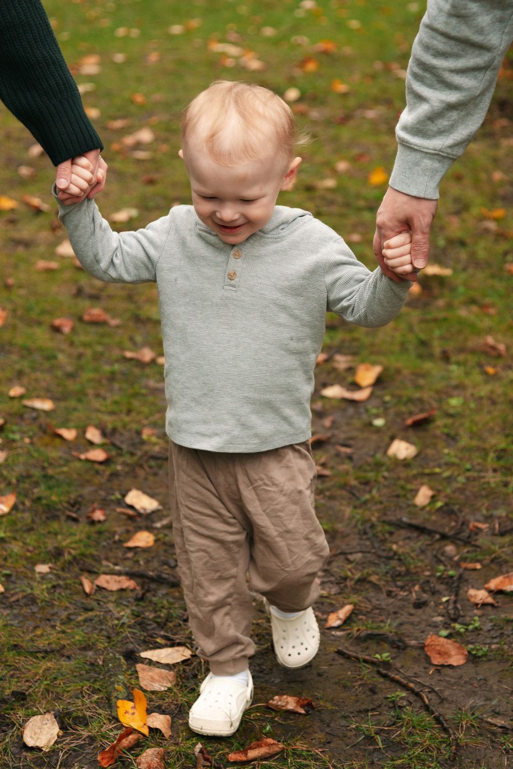 A small child in grey sweater and khaki pants holding hands while walking outdoors.
