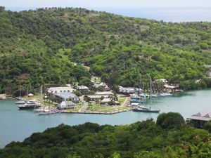 Aerial view of a tropical harbor with sailboats docked near lush green hills and colonial buildings in Antigua.