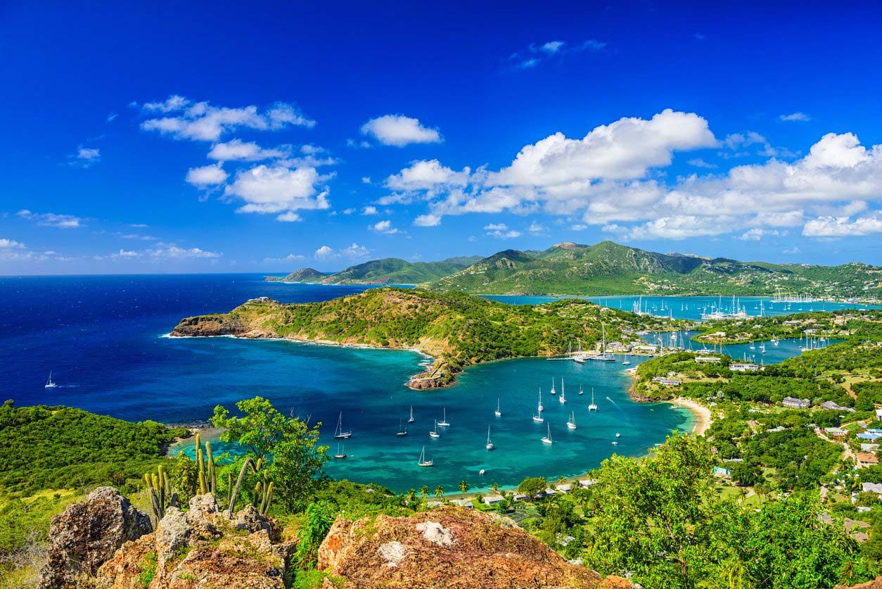 Aerial view of a stunning Caribbean bay with turquoise waters, sailboats, and lush green hills under a bright blue sky.