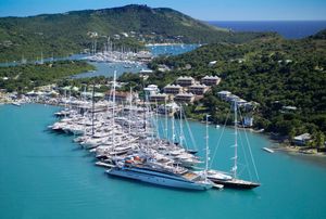 Aerial view of a luxury yacht marina with turquoise waters, lush green hills, and numerous sailboats docked in a tropical harbor.