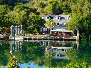 Elegant lakeside villa with stone columns, lush greenery, and perfect water reflections on a serene pond.