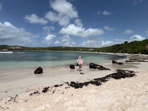 Woman in pink standing on a pristine white sand beach with crystal clear turquoise water under a sunny blue sky.