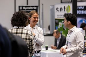 Three professionals networking at a trade show booth with Symétrie and SPT company banners visible in the background.